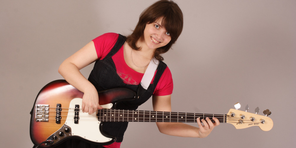 Featured image for "Bass Lessons" page on MusicLessonsNashville.com depicting young woman playing a sunburst Fender Jazz 4-string bass.