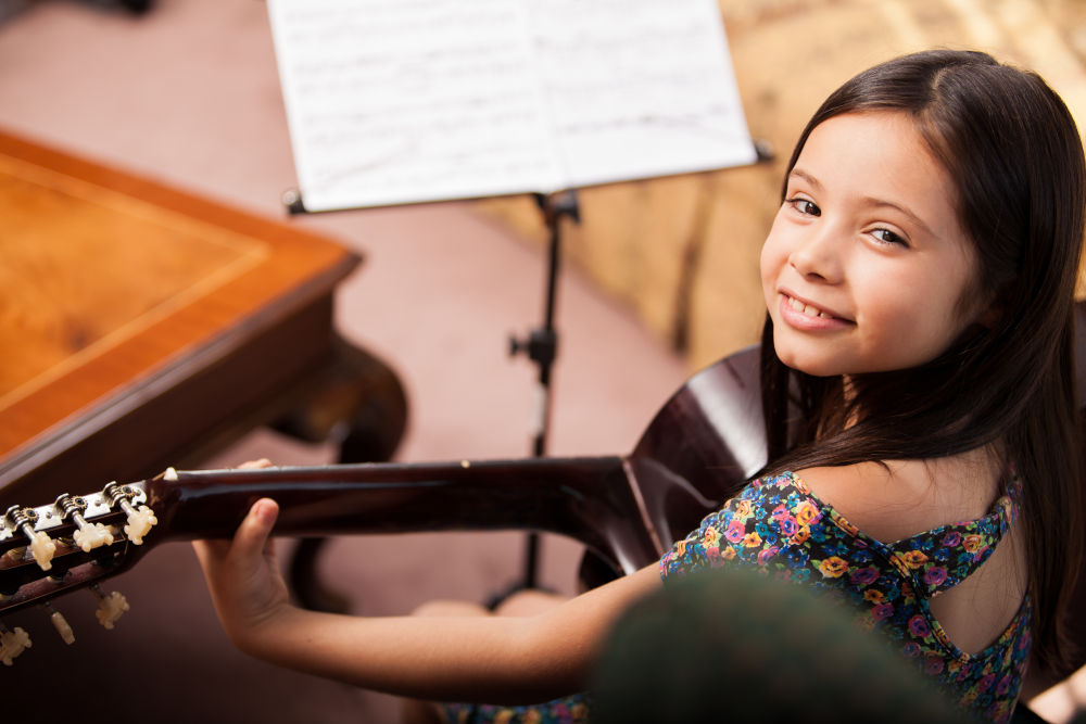 Featured image for "Guitar Lessons" page on MusicLessonsNashville.com depicting young girl sitting down in front of a music stand while playing nylon-string classical guitar.