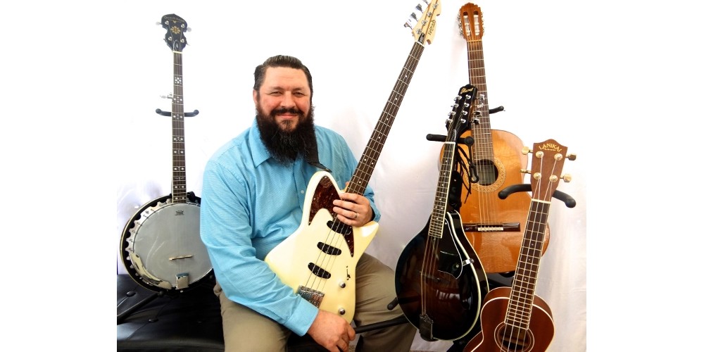 Featured image for home page of MusicLessonsNashville.com depicting instructor Ryan Byrne posing with multiple instruments: bass, guitar, banjo, mandolin, and ukulele.